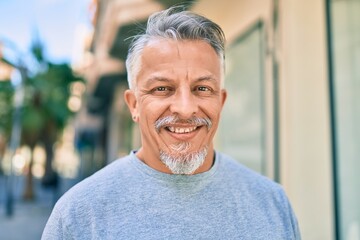 Middle age hispanic grey-haired man smiling happy standing at the city.