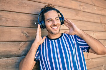 Young hispanic man smiling happy listening to music using headphones at the city.