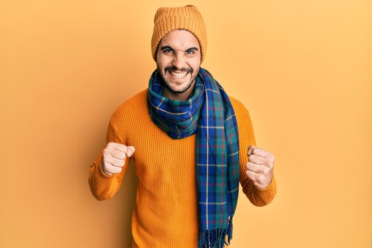Young hispanic man wearing wool sweater and winter scarf celebrating surprised and amazed for success with arms raised and eyes closed