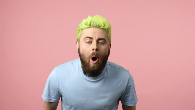Extremely surprised shocked man with dyed bright green hair widely open mouth looking at camera with big eyes, expressing astonishment. Indoor studio shot isolated on pink background