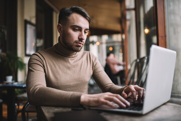 Serious man typing on laptop in cafe