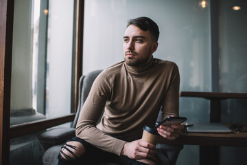 Positive man with takeaway coffee using smartphone