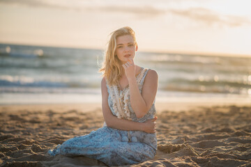 beautiful girl in a blue dress sitting by the ocean. enchanted view of the beach. romance by the ocean
