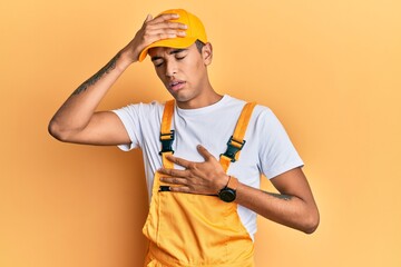 Young handsome african american man wearing handyman uniform over yellow background touching forehead for illness and fever, flu and cold, virus sick
