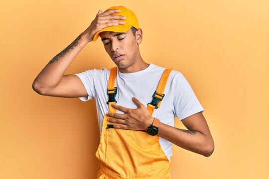 Young handsome african american man wearing handyman uniform over yellow background touching forehead for illness and fever, flu and cold, virus sick