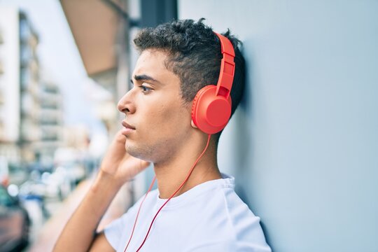 Young latin man with serious expression listening to music using headphones at the city.