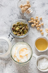 Some glass jars full of granola ingredients over a rustic white grey background.