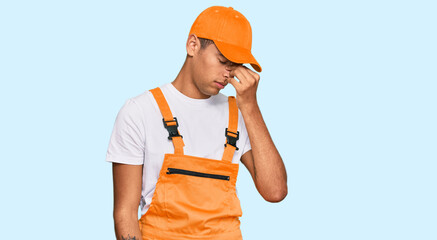 Young handsome african american man wearing handyman uniform tired rubbing nose and eyes feeling...