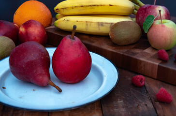 Fresh organic fruit on a white plate and a wooden  cutting board.