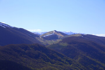 Obraz premium Range of mountains at the beginning of spring, between the green of the new vegetation and the residual snow in dissolution