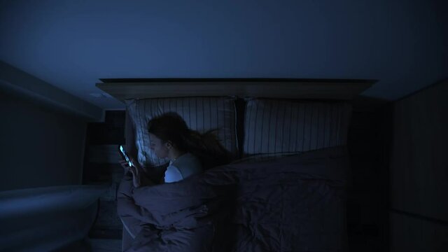 Top view of one woman in bed at night looking at her smartphone, female insomnia problem, woman can not get asleep at night, lonely girl in bed at night.