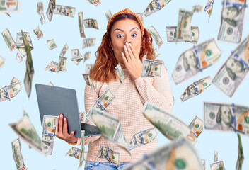 Young latin woman holding laptop covering mouth with hand, shocked and afraid for mistake....