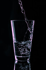 In a transparent glass on a black background pouring water from the bottle.
