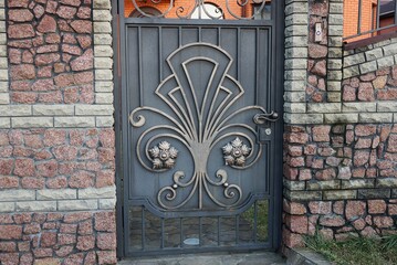  metal closed door with a  forged pattern and a part of a stone wall of a fence on the street