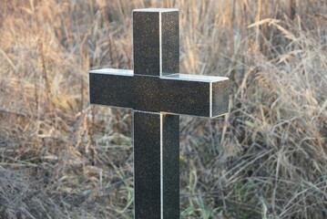 one black marble cross on an old grave in a cemetery overgrown with dry gray grass