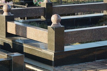 part of the gray marble fence stands on black slabs at the grave in the cemetery