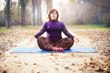 Fat middle-aged woman practicing yoga in the autumn park