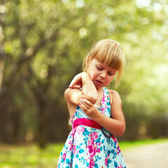 Close-up of a little tear-stained girl in a dress who hurt her hand in the park.