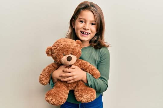 Little beautiful girl hugging teddy bear smiling and laughing hard out loud because funny crazy joke.