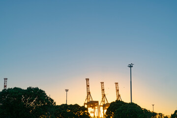 Container cranes on Port of Tauranga facility backlit by rising sun.