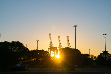 Container cranes on Port of Tauranga facility backlit by rising sun at Sulphur Point in city.