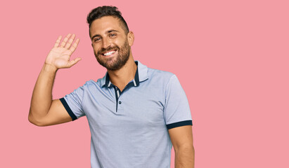 Handsome man with beard wearing casual clothes waiving saying hello happy and smiling, friendly welcome gesture