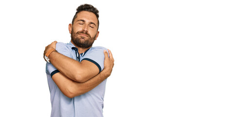 Handsome man with beard wearing casual clothes hugging oneself happy and positive, smiling confident. self love and self care