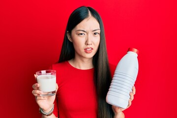 Young chinese woman drinking a glass of fresh milk clueless and confused expression. doubt concept.