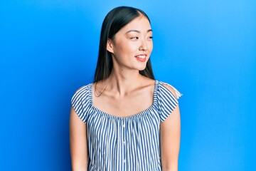 Fototapeta premium Young chinese woman wearing casual striped t-shirt looking away to side with smile on face, natural expression. laughing confident.