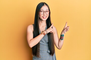 Young chinese woman wearing business dress and glasses smiling and looking at the camera pointing with two hands and fingers to the side.
