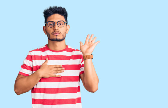 Handsome latin american young man wearing casual clothes and glasses swearing with hand on chest and open palm, making a loyalty promise oath