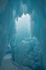 A walkway through ice. Blue and white icicles are hanging from above and the pathway is covered in snow.