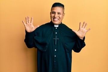Young latin priest man standing over yellow background showing and pointing up with fingers number...