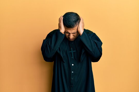 Young latin priest man standing over yellow background suffering from headache desperate and stressed because pain and migraine. hands on head.