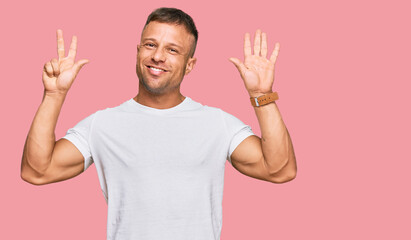 Handsome muscle man wearing casual white tshirt showing and pointing up with fingers number eight while smiling confident and happy.