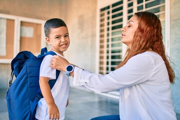 Adorable latin student boy and mom at school. Mother preparing kid putting up backpack.