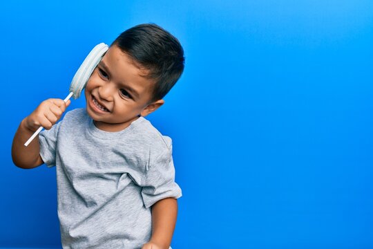 Adorable latin toddler eating delicious lollipop over isolated blue background.