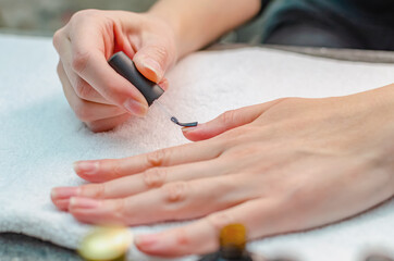 A woman applies a primer to her nails before applying varnish. Close-up of a hand.