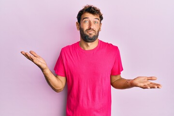 Handsome man with beard wearing casual pink tshirt over pink background clueless and confused...