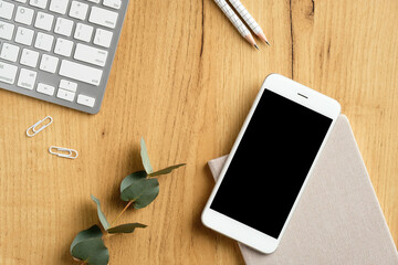 Modern office desk top view. Flat lay smartphone with empty screen mockup, pc keyboard, eucalyptus...