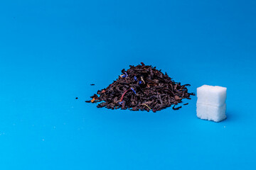Heap of black tea and cubes of white sugar on a blue background.