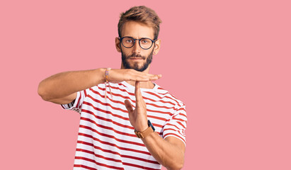 Handsome blond man with beard wearing casual clothes and glasses doing time out gesture with hands,...