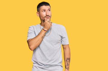 Handsome man with tattoos wearing 90s style with hand on chin thinking about question, pensive...