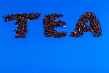 On a blue background the inscription TEA consisting of black tea leaves.