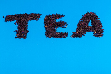 On a blue background the inscription TEA consisting of black tea leaves.