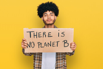Young african american man with afro hair holding there is no planet b banner thinking attitude and sober expression looking self confident