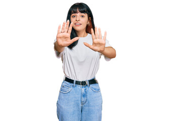 Young hispanic girl wearing casual clothes afraid and terrified with fear expression stop gesture...