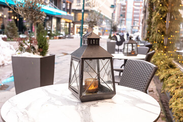 Lantern in the snow on the table. Street cafe interior
