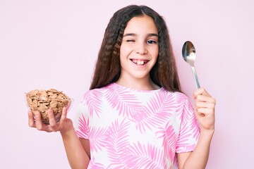 Cute hispanic girl holding cornflakes and spoon winking looking at the camera with sexy expression,...