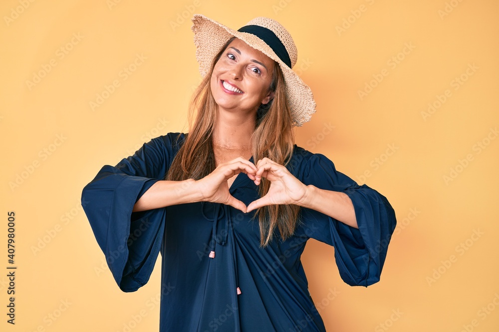 Canvas Prints Middle age hispanic woman wearing summer hat smiling in love showing heart symbol and shape with hands. romantic concept.